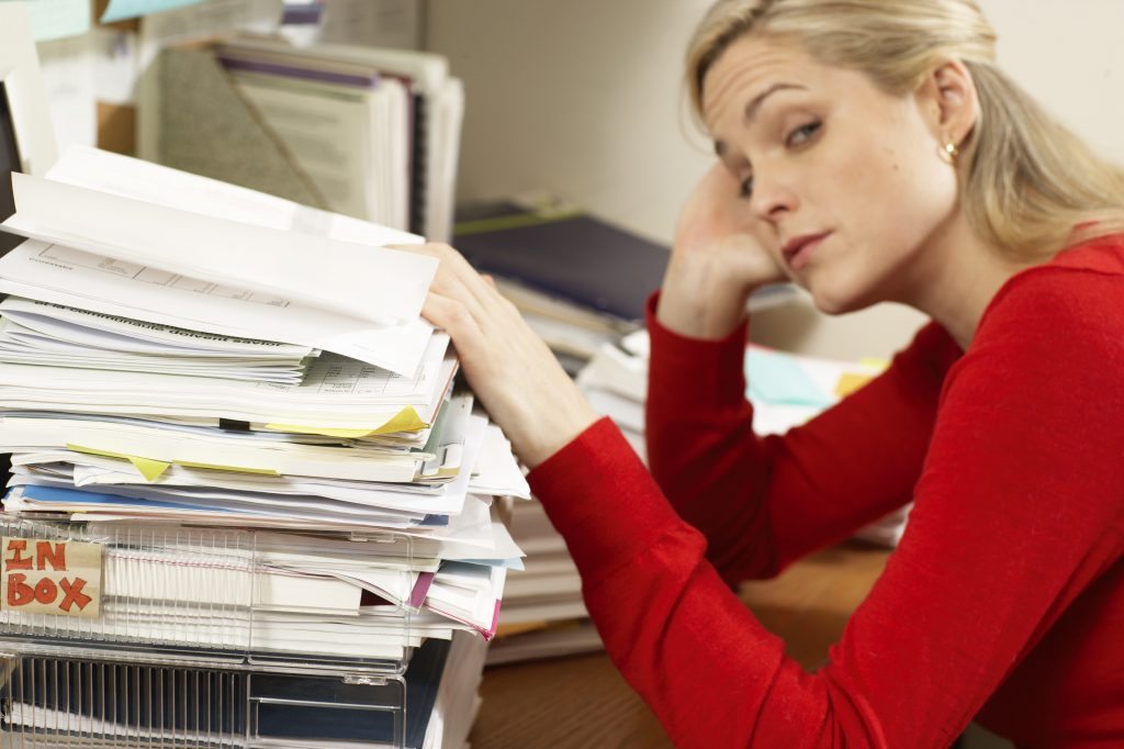 Female office worker with hand resting on paperwork stacked on in tray